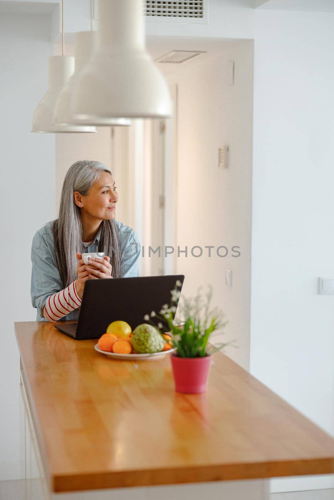 Smiling woman drinking coffee and using laptop at home by Yaroslav_astakhov