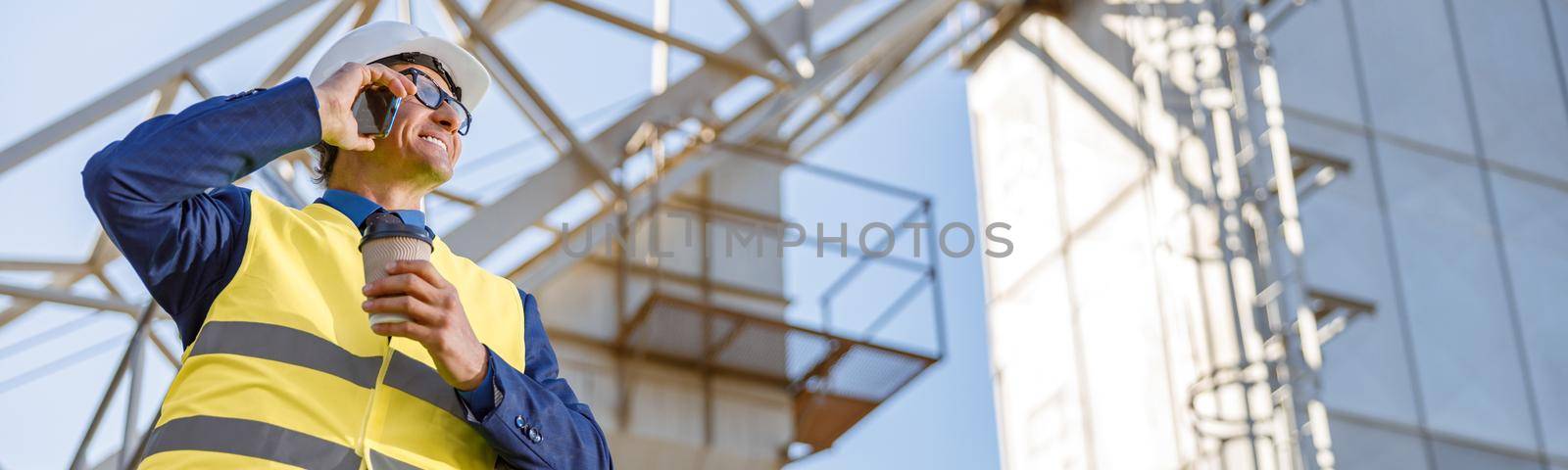 Joyful matured man engineer having phone conversation and smiling while holding cup of coffee