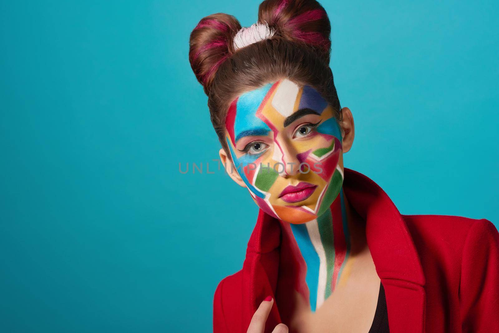 Funky and stylish model wearing in red clothes, has creative, colorful pop art make up. Confident girl has bow hairstyle, looks like comic character. Woman looking at camera.