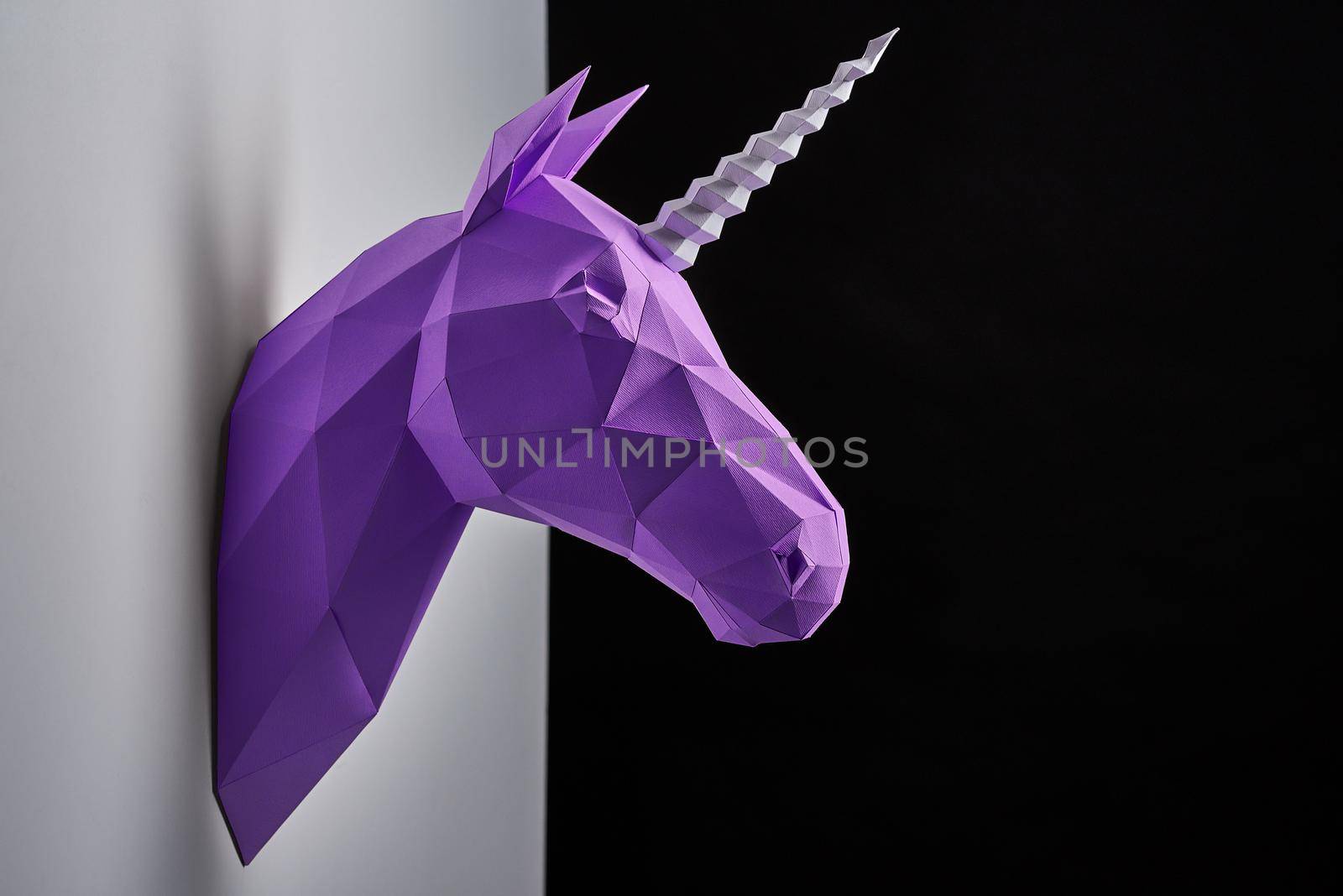 Horizontal shoot of violet unicorn's head hanging on grey shadowed wall. by SerhiiBobyk