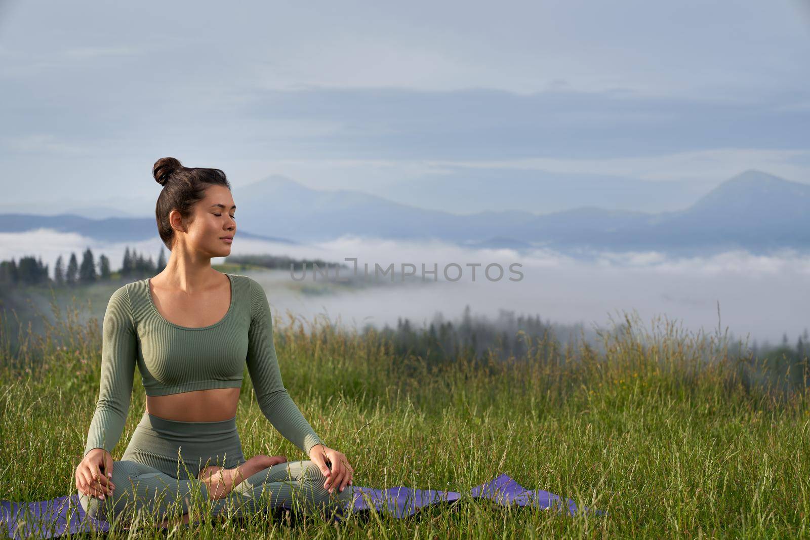 Young woman with dark hair practising meditation in lotus position with beautiful mountains on background. Concentration and relaxation concept.