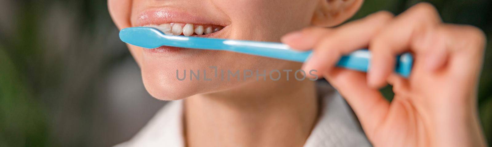 Closeup of young woman in white bathrobe brushing her teeth while standing in front of a mirror. Dental health care concept