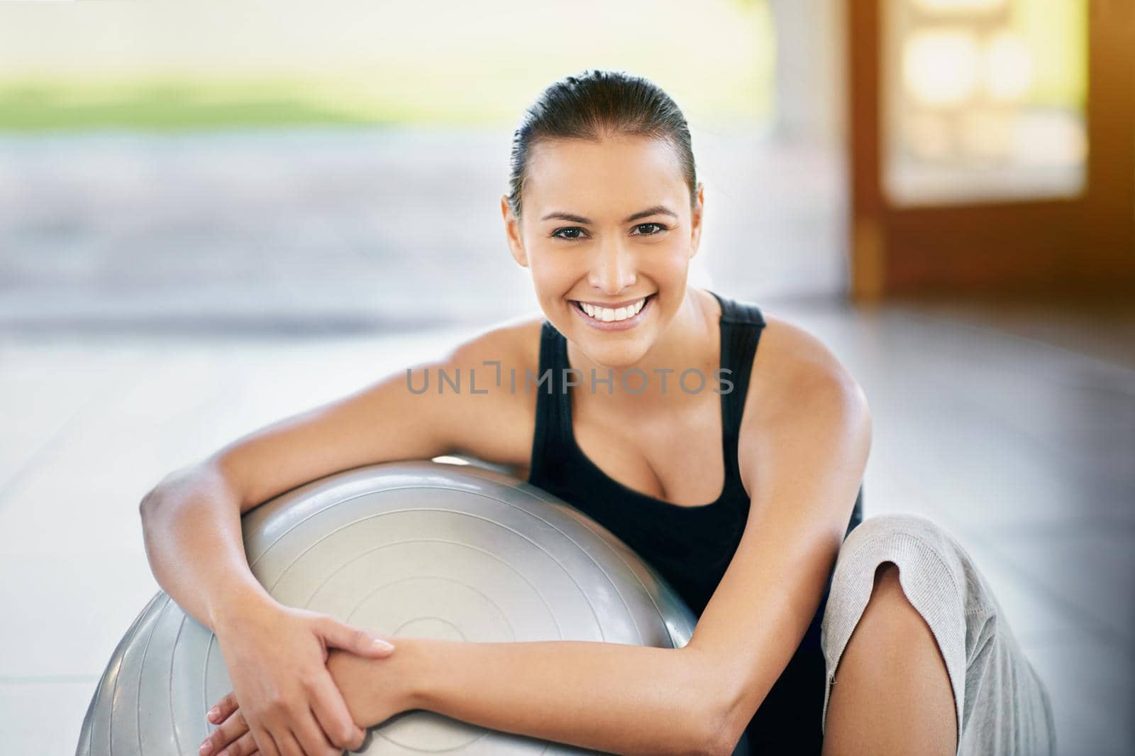 What a great workout. Cropped portrait of a young woman sitting against her exercise ball. by YuriArcurs