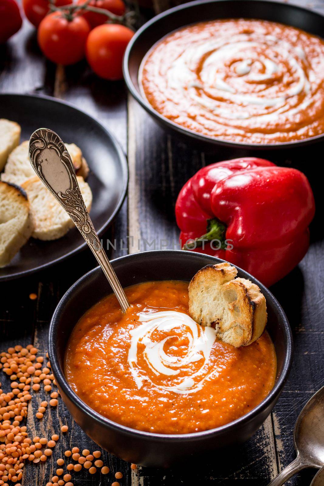 Delicious pumpkin soup with heavy cream on dark rustic wooden table with red bell pepper, bread toasts, lentil, tomatoes