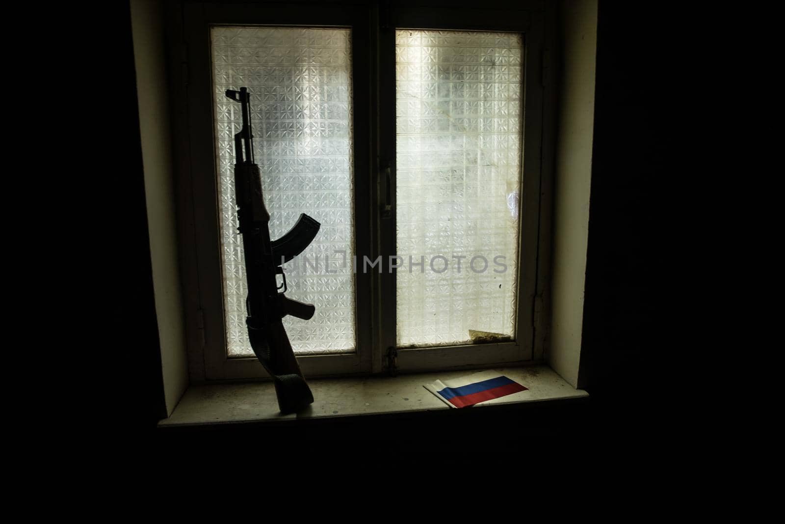 Conceptual photo of war between Russia and Ukraine. Russian flag and soviet gun on windowsill at night. Old creepy room with window. Explosion outside.