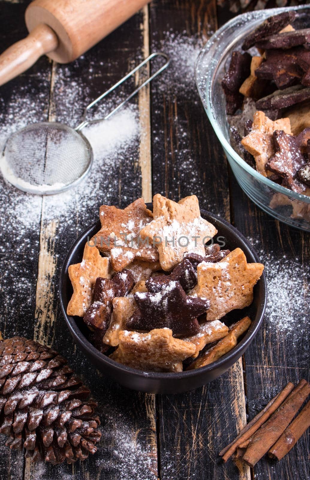 Assorted christmas ginger cookies on plate with cinnamon sticks, pinecones over dark wooden table. Six pointed star cookies