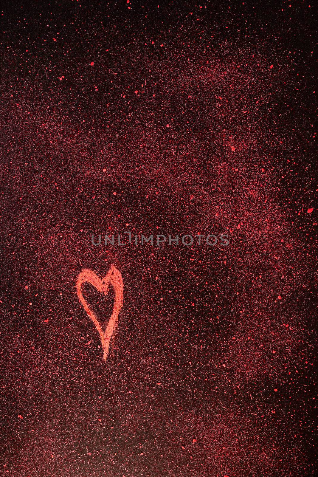 Red heart shape drawn with red chalk  on black background with red small pieces of chalk