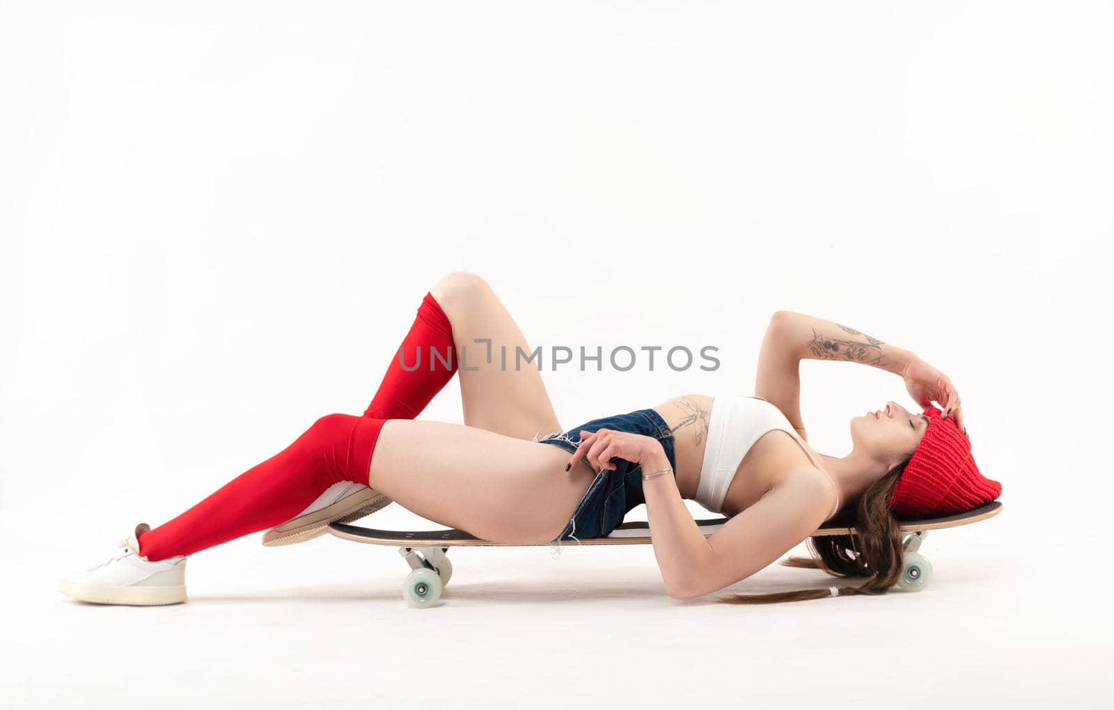 the skater girl lying on a longboard in bright fashionable clothes on a white background