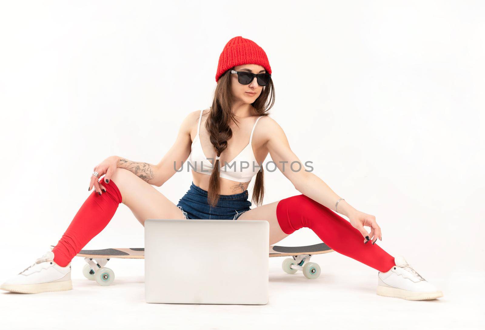 the girl in a red hat and red socks is sitting on a longboard with a laptop on a white background