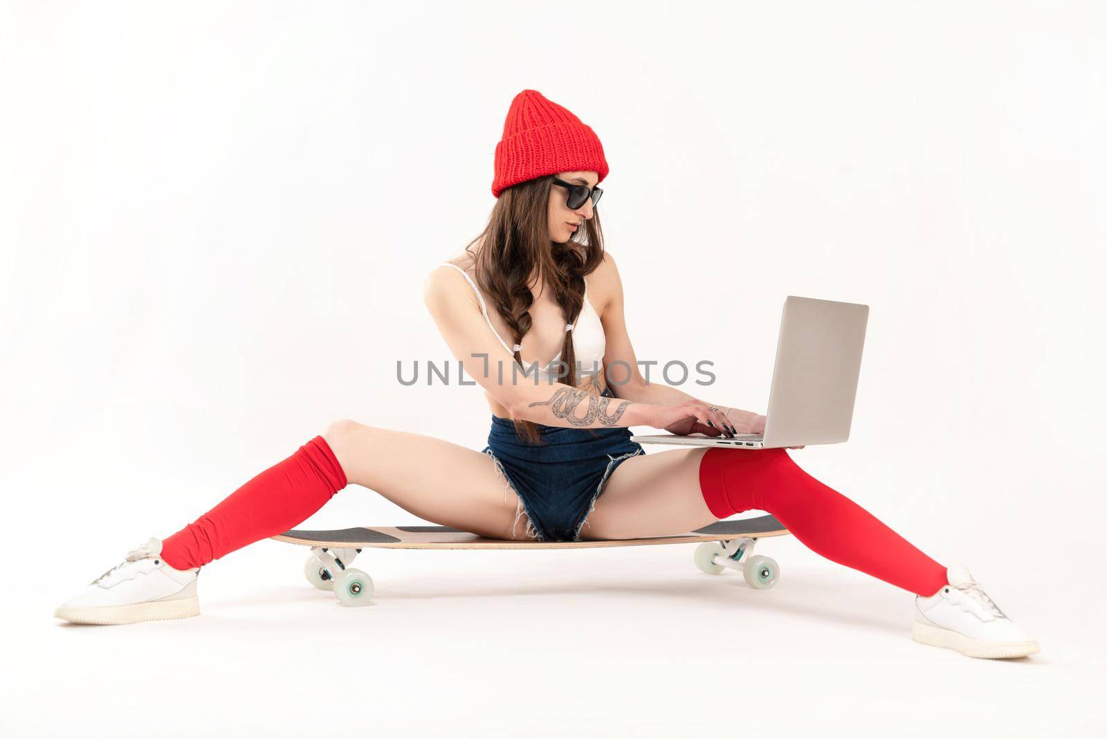 girl in a red hat and red socks is sitting on a longboard with a laptop on a white background by Rotozey