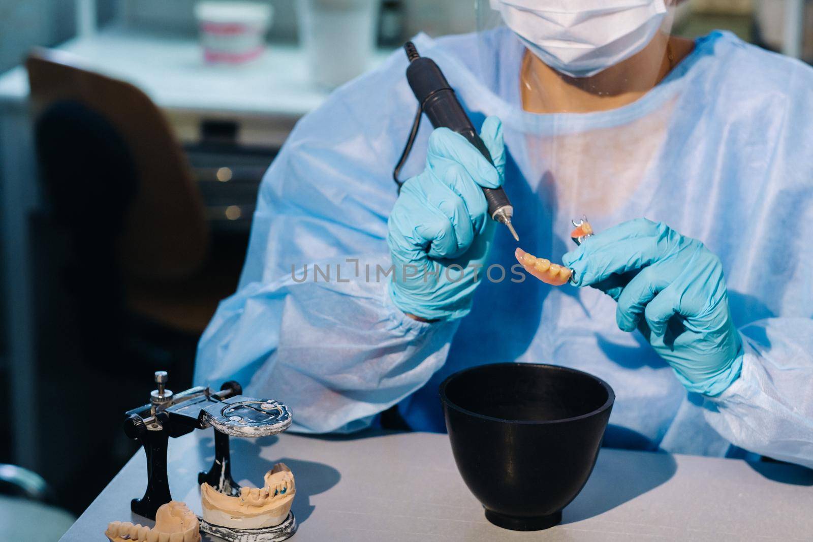 A dental technician in protective clothing is working on a prosthetic tooth in his laboratory.