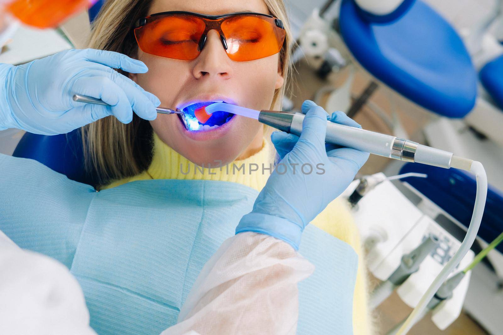 A female patient in dental glasses treats teeth at the dentist with ultraviolet light. dental fillings by Lobachad