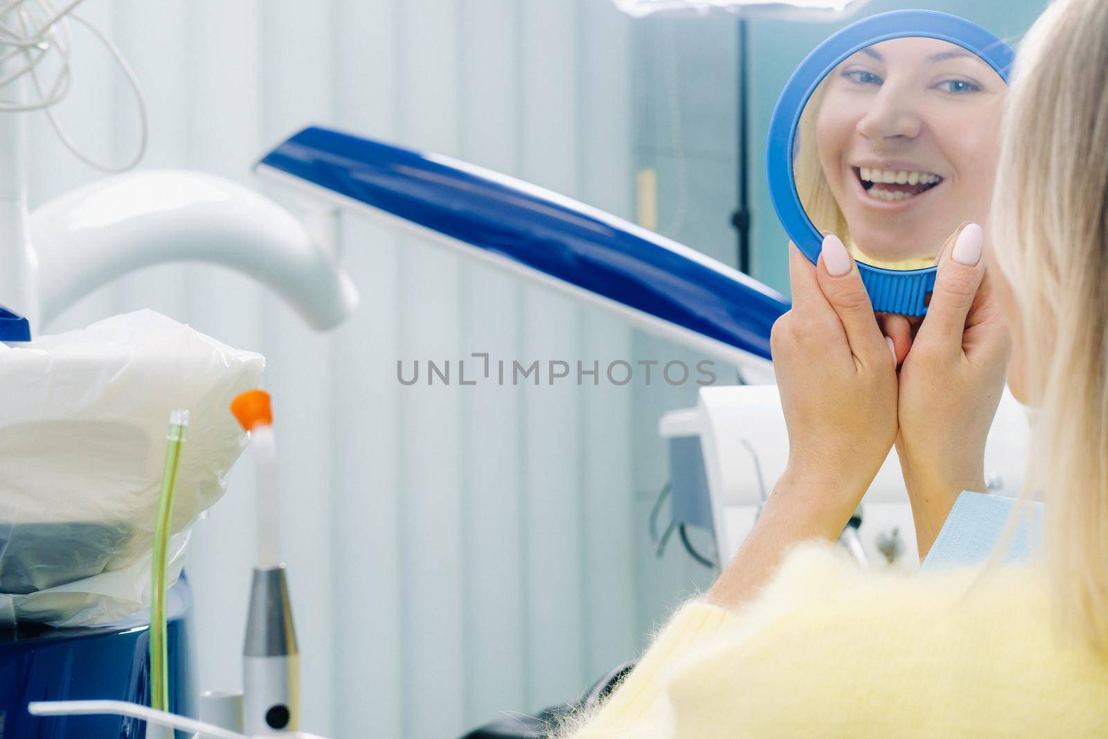 The girl smiles and looks in the mirror in the dentist's office by Lobachad