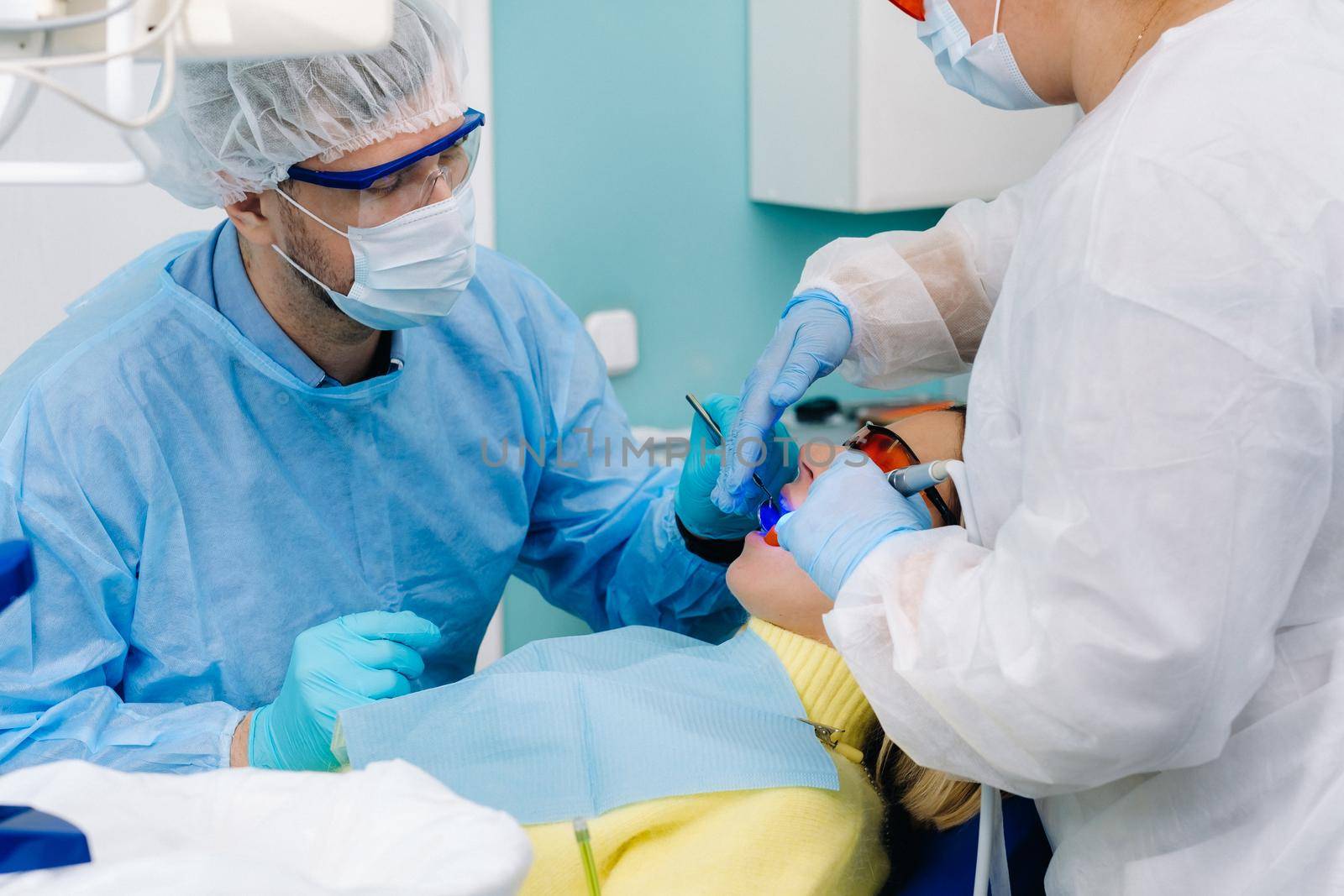 A female patient in dental glasses treats teeth at the dentist with ultraviolet light. dental fillings by Lobachad