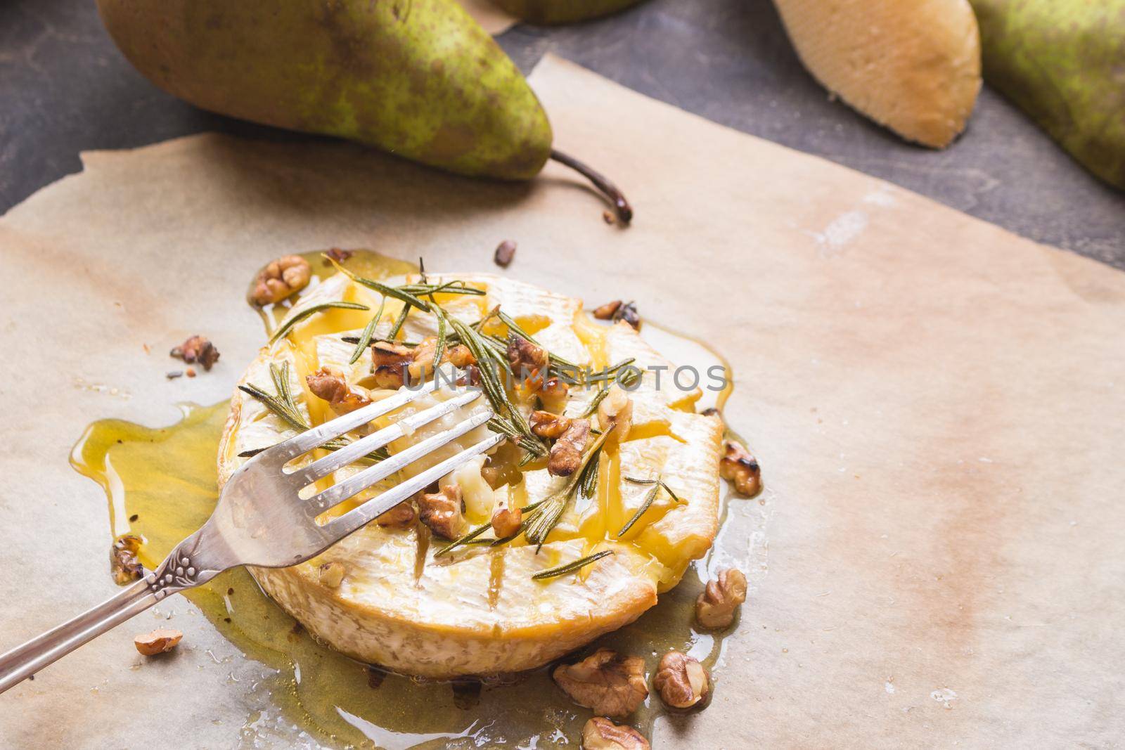 Piece of baked camambert on a fork. Delicious baked cheese with honey, walnuts, herbs and pears