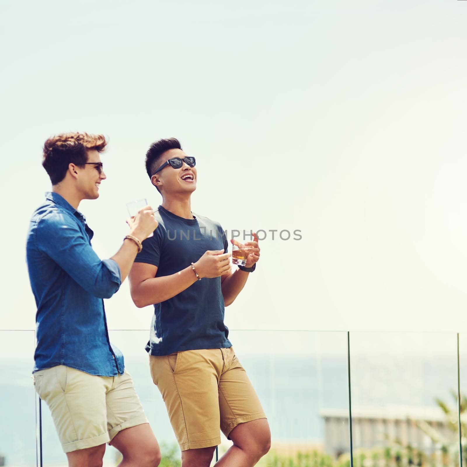 Shot of two handsome young men having drinks and relaxing outdoors while on holiday.