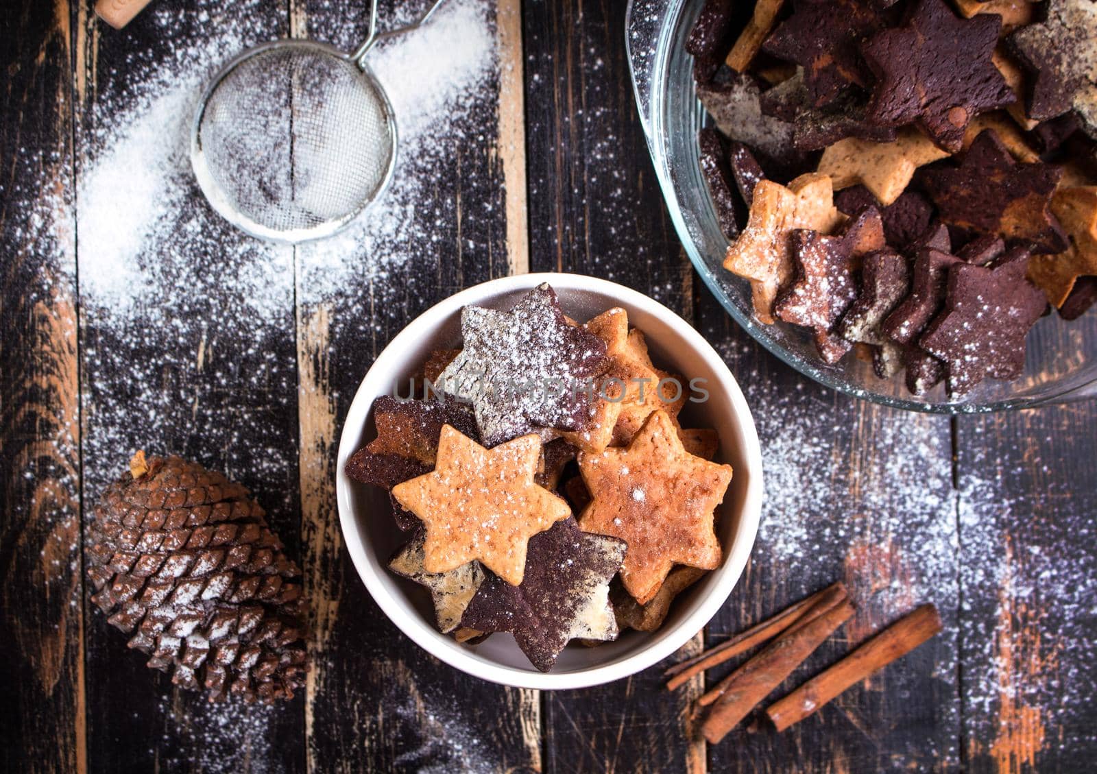 Assorted christmas ginger cookies on plate with cinnamon sticks, pinecones over dark wooden table. Six pointed star cookies