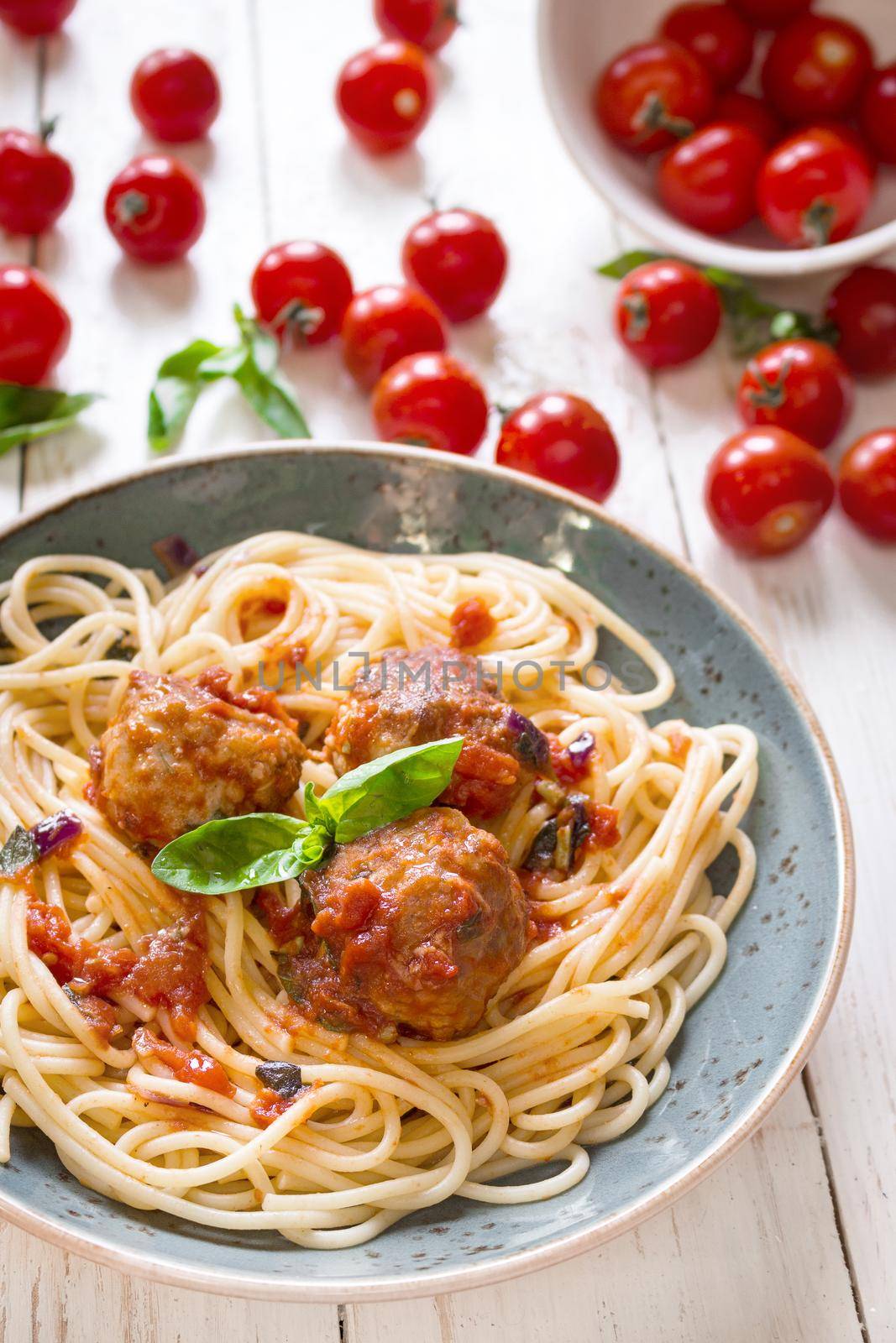 Close-up of delicious spaghetti with meatballs and tomato sauce on a plate. Serving on a white rustic wooden table. An Italian-American dish. Selective focus
