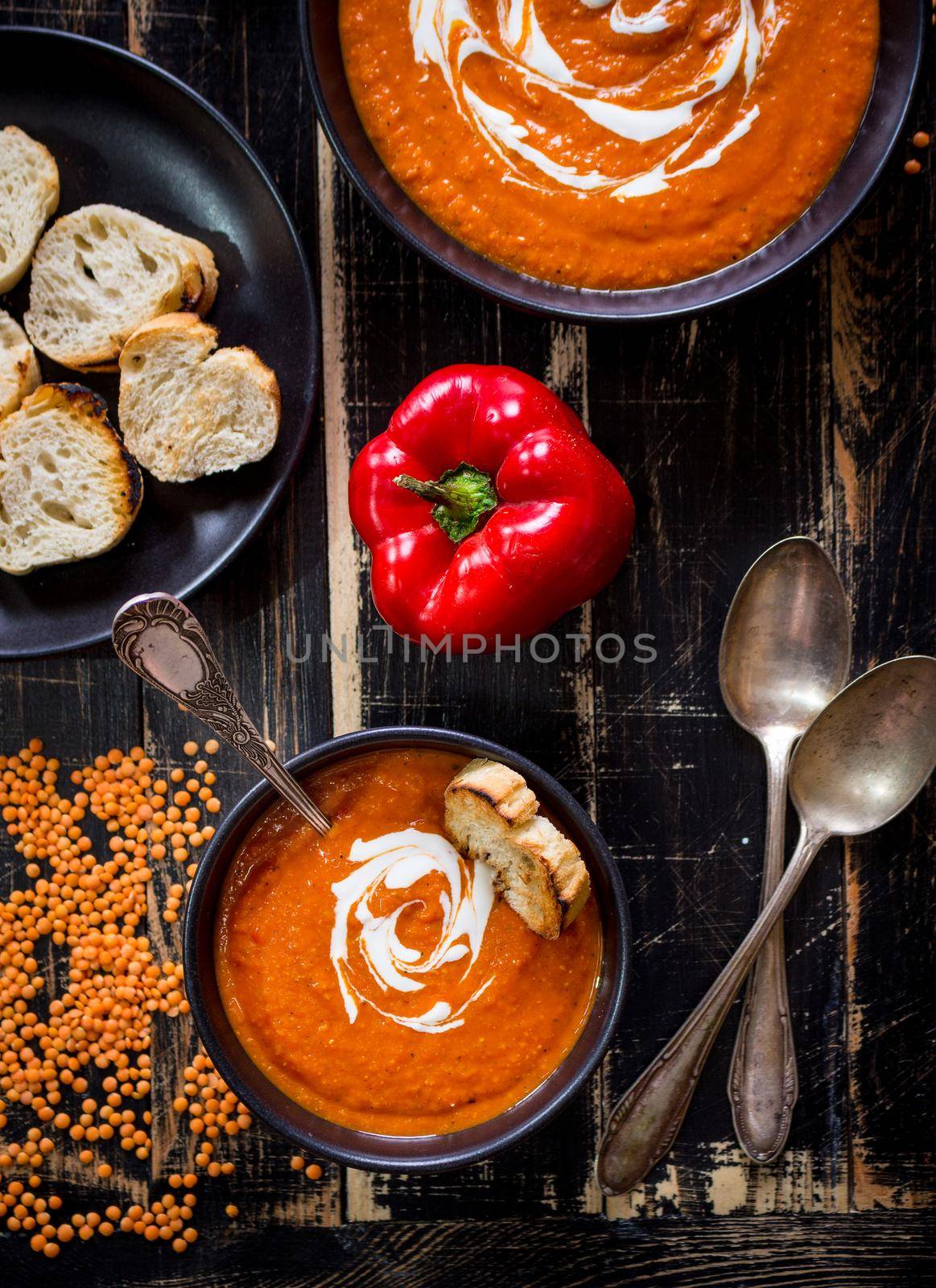 Delicious pumpkin soup with heavy cream on dark rustic wooden table with red bell pepper, bread toasts, lentil. Top view