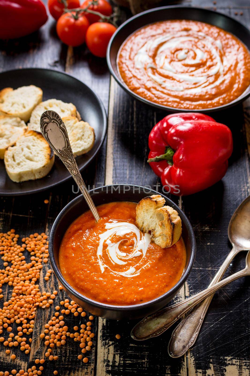 Delicious pumpkin soup with heavy cream on dark rustic wooden table with red bell pepper, bread toasts, lentil, tomatoes