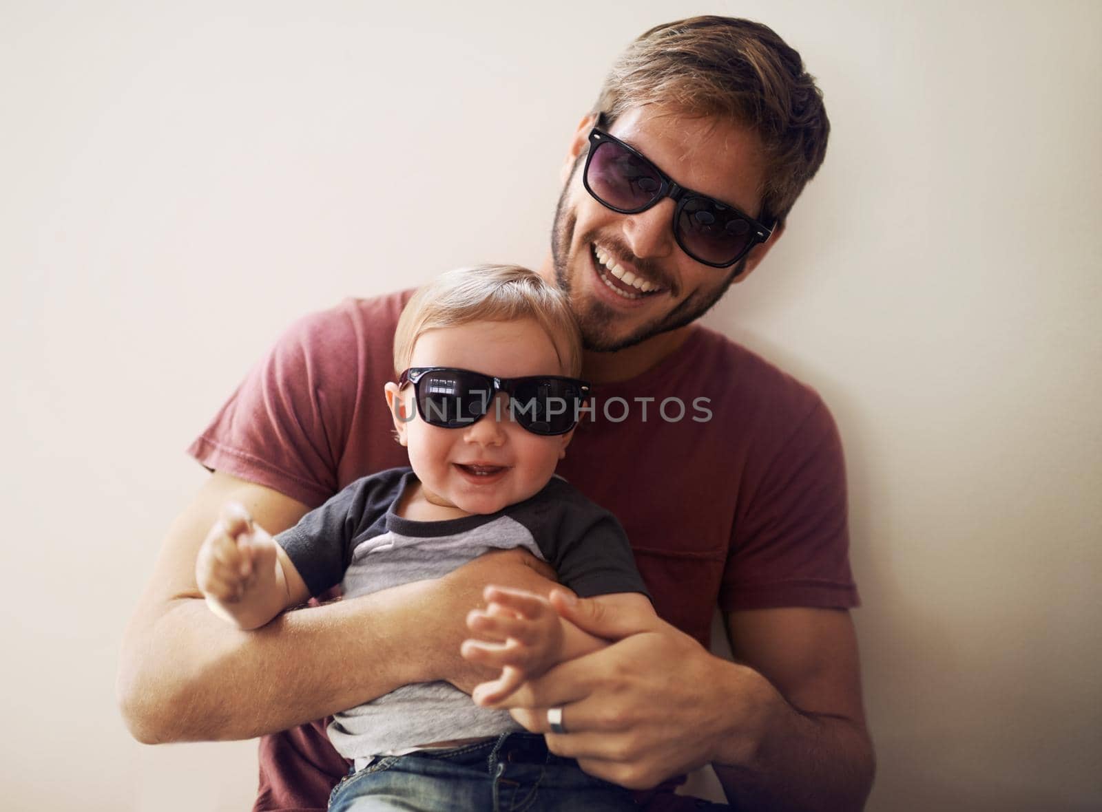 Coolness runs in this family. A young father and his infant son wearing matching sunglasses and laughing. by YuriArcurs