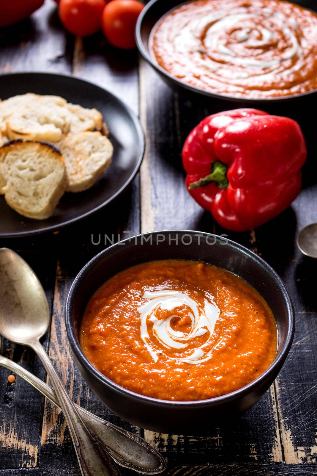 Delicious pumpkin soup with heavy cream on dark rustic wooden table with red bell pepper, bread toasts, lentil, tomatoes