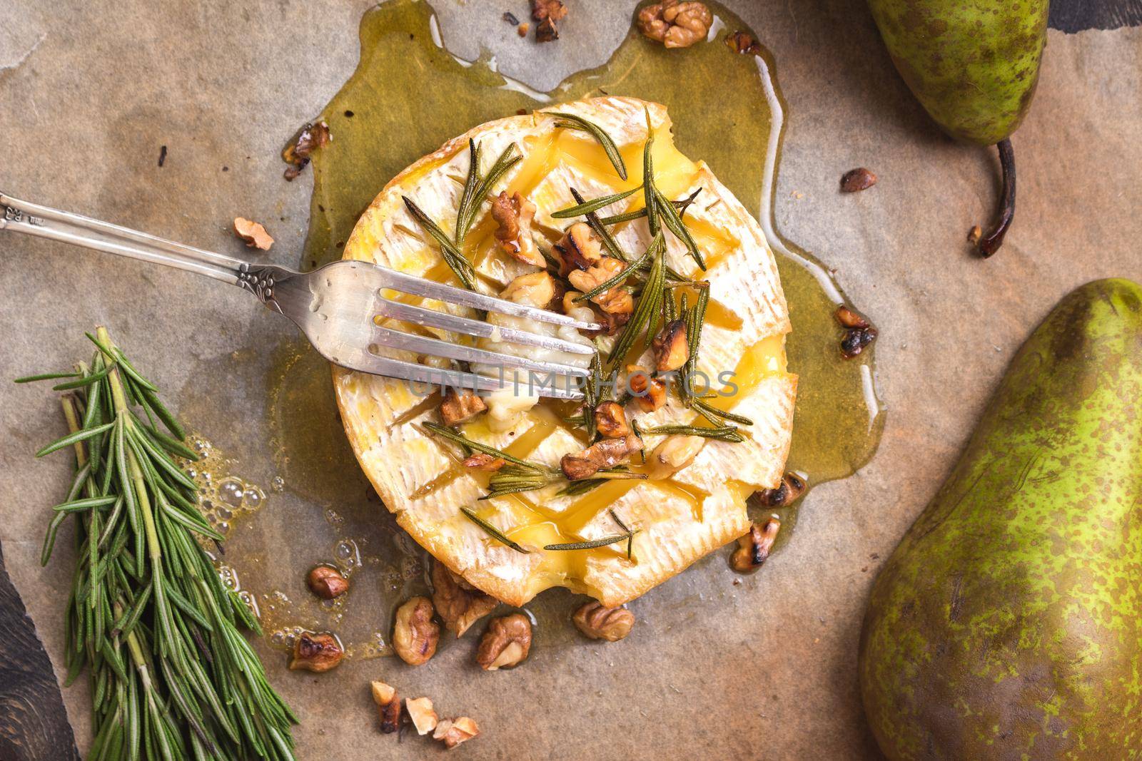 Delicious beautiful baked camembert with fork. Cheese with honey, walnuts, herbs and pears