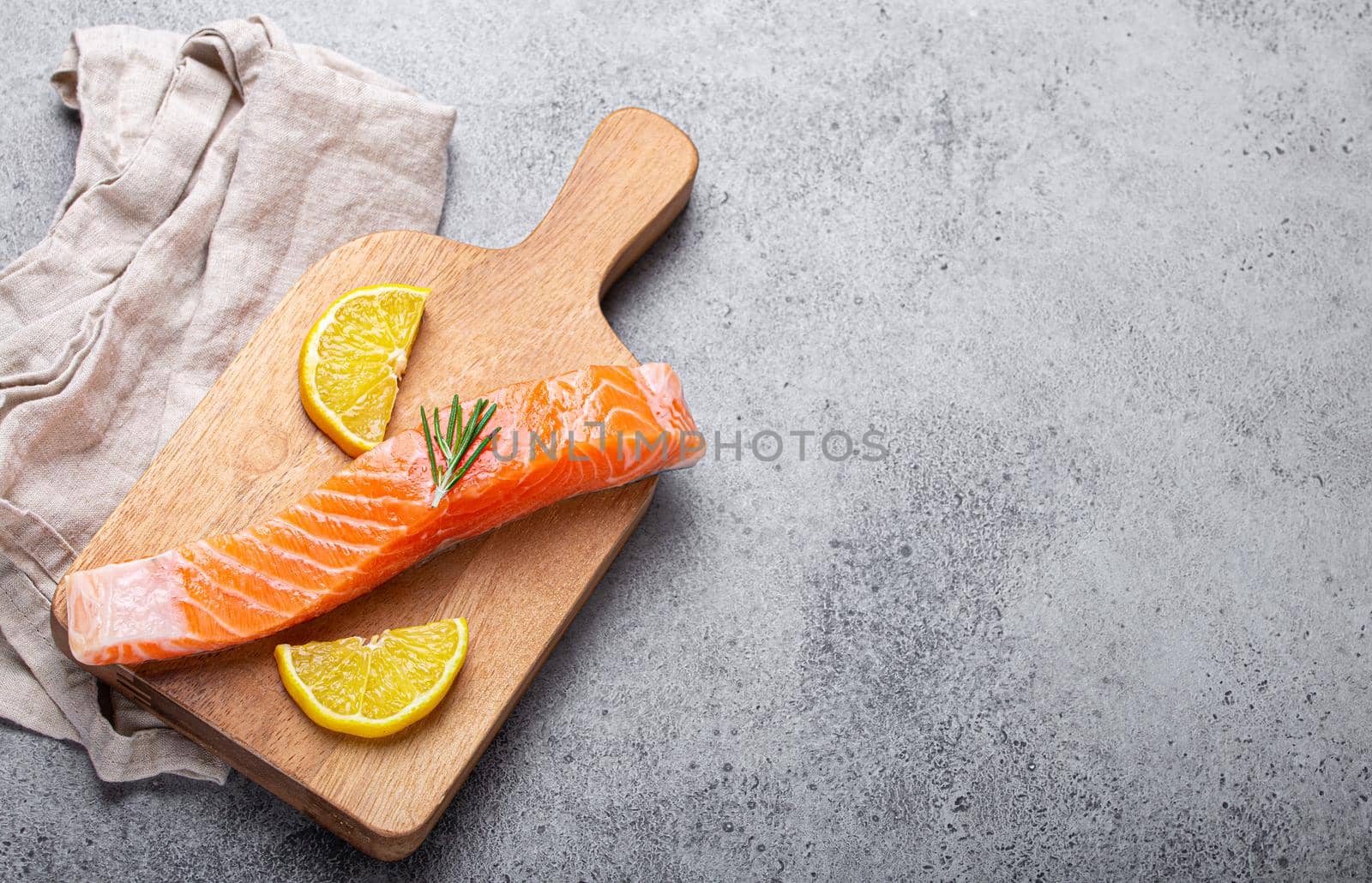 Raw salmon fish fillet with lemon wedges and rosemary on wooden cutting board by its_al_dente