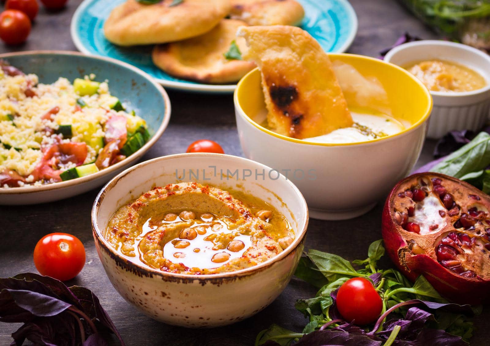 Table served with middle eastern traditional vegetarian dishes. Hummus, tahini, pitta, couscous salad and buttermilk dip with olive oil. Dinner party