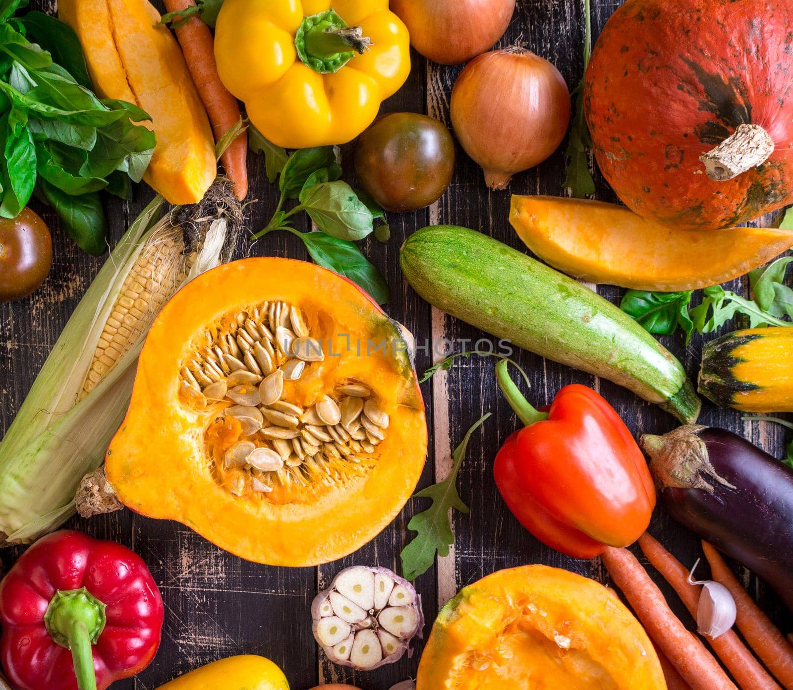 Close up of fresh vegetables on a old rustic dark textured table. Autumn background. Healthy eating. Sliced pumpkin, zucchini, squash, bell peppers, carrots, onions, cut garlic, tomatoes, eggplant, corn cob, rucola and basil. Top view