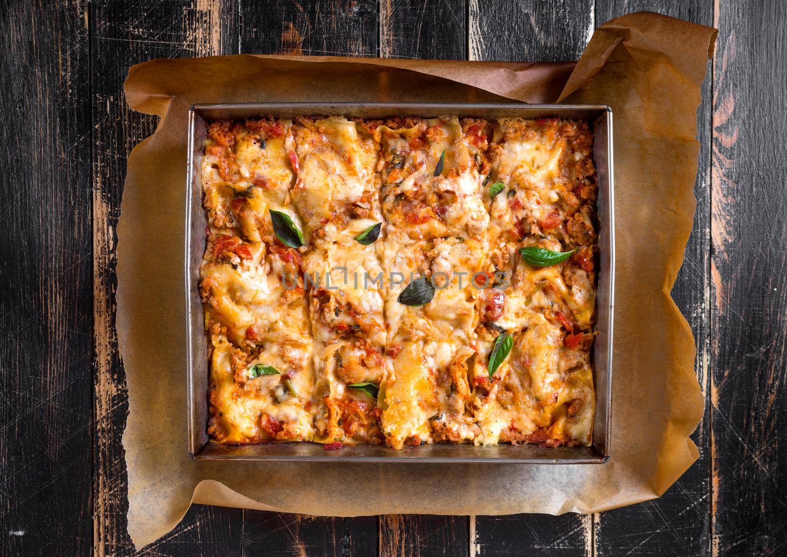 Top view of a delicious traditional italian lasagna made with minced beef bolognese sauce topped with basil leafs served on a rustic dark wooden table