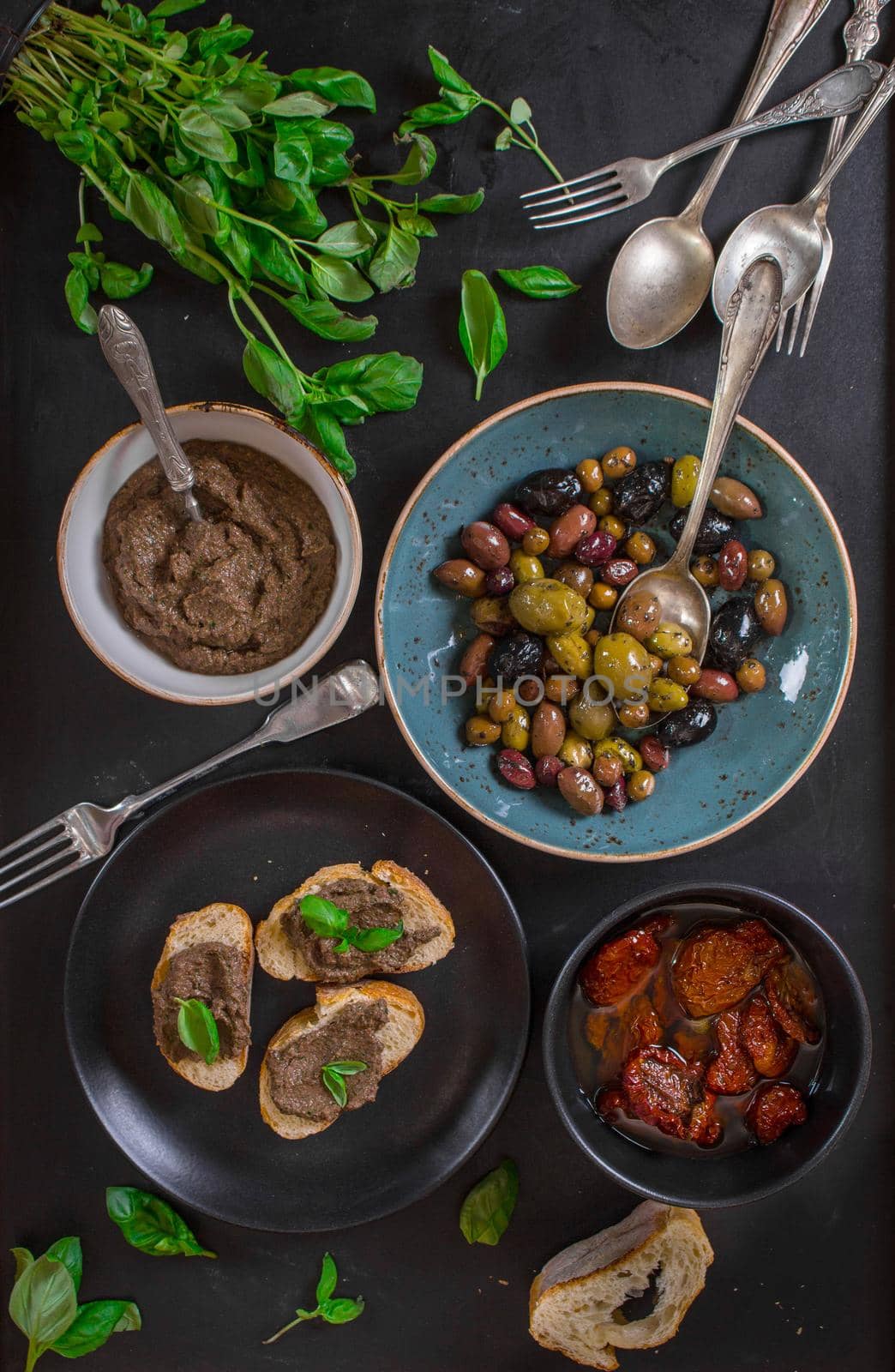 Table served with bread, tapenade, assorted olives, dried tomatoes in olive oil and basil. Dinner table with french provence appetizers and canapes