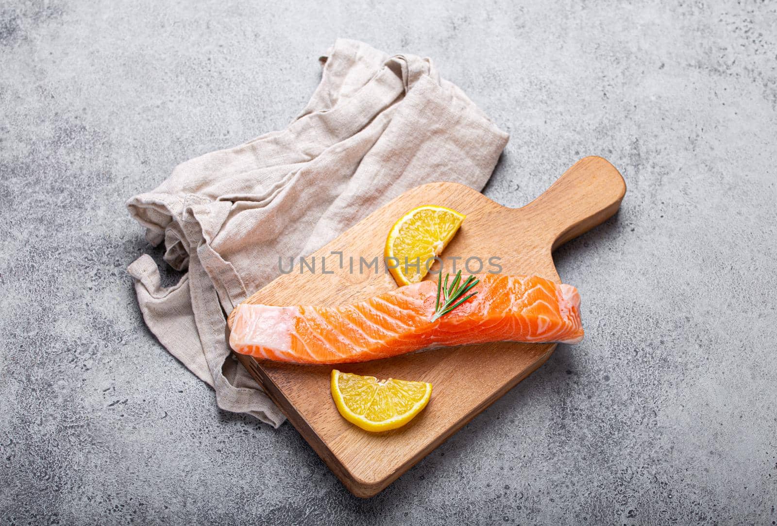 Raw salmon fish fillet with lemon wedges and rosemary on wooden cutting board by its_al_dente