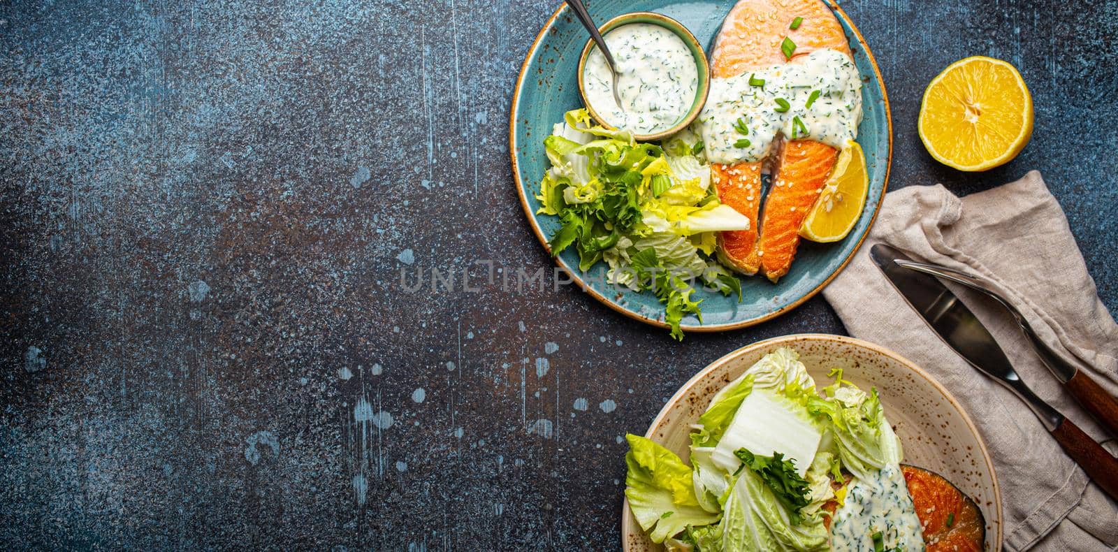 Healthy food meal grilled salmon steaks with dill sauce and salad leafs on two plates on rustic concrete stone background table flat lay from above, diet healthy nutrition dinner, space for text