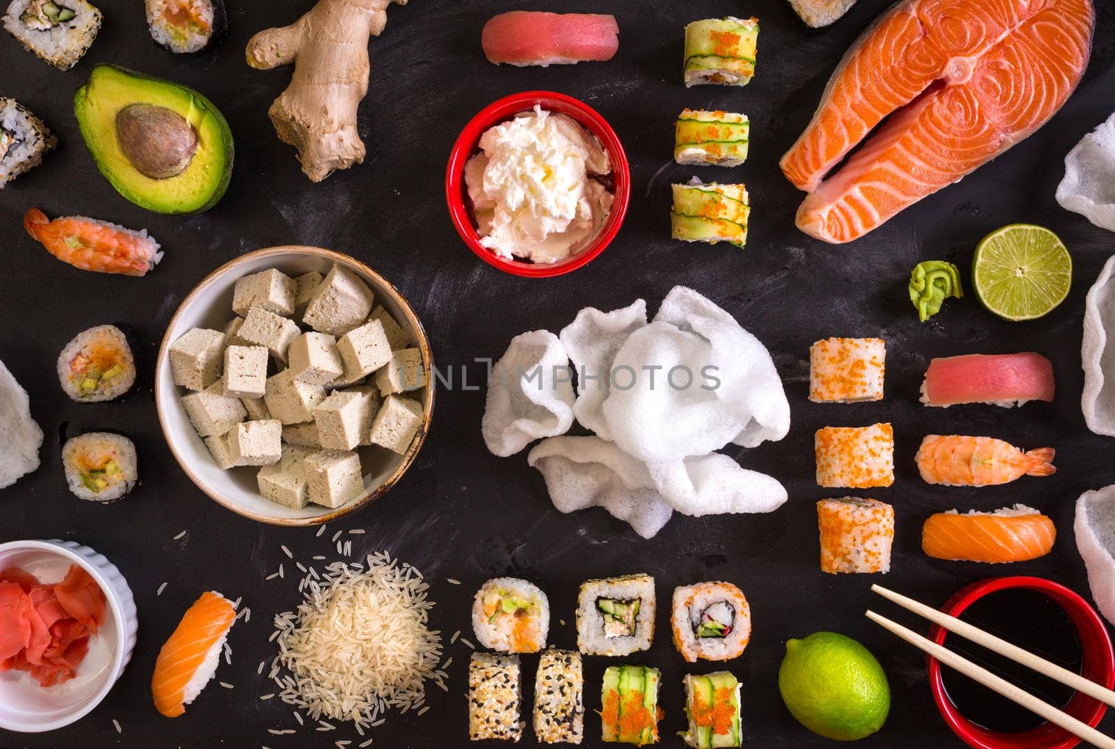 Set of traditional japanese food on a dark background. Sushi rolls, nigiri, raw salmon steak, rice, cream cheese, avocado, lime, pickled ginger (gari), raw ginger, wasabi, soy sauce, nori, сhopsticks. Asian food frame. Dinner party. Space for text....