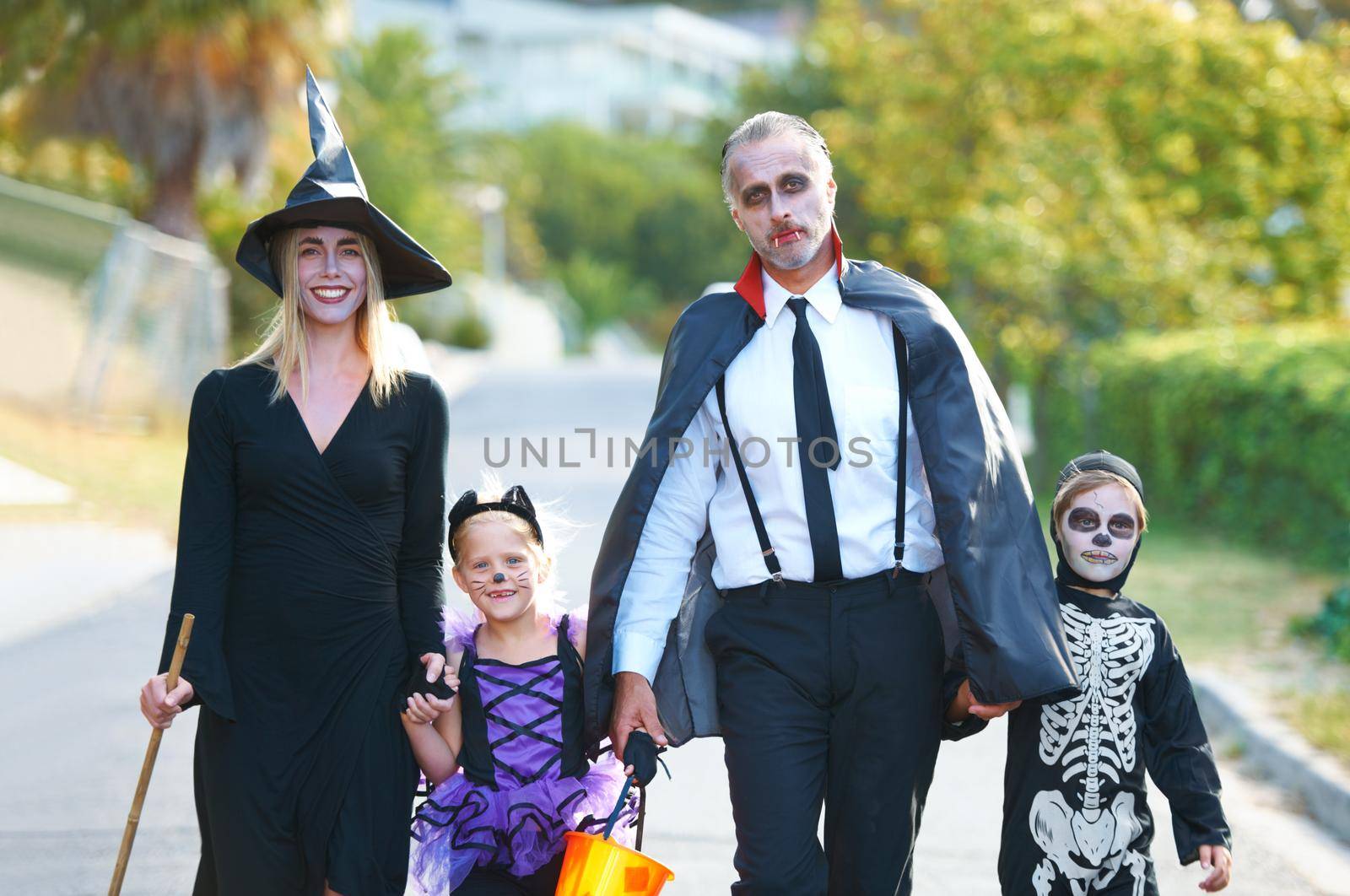 Celebrating the fun together. A cute family dressed up for Halloween walking down their street. by YuriArcurs