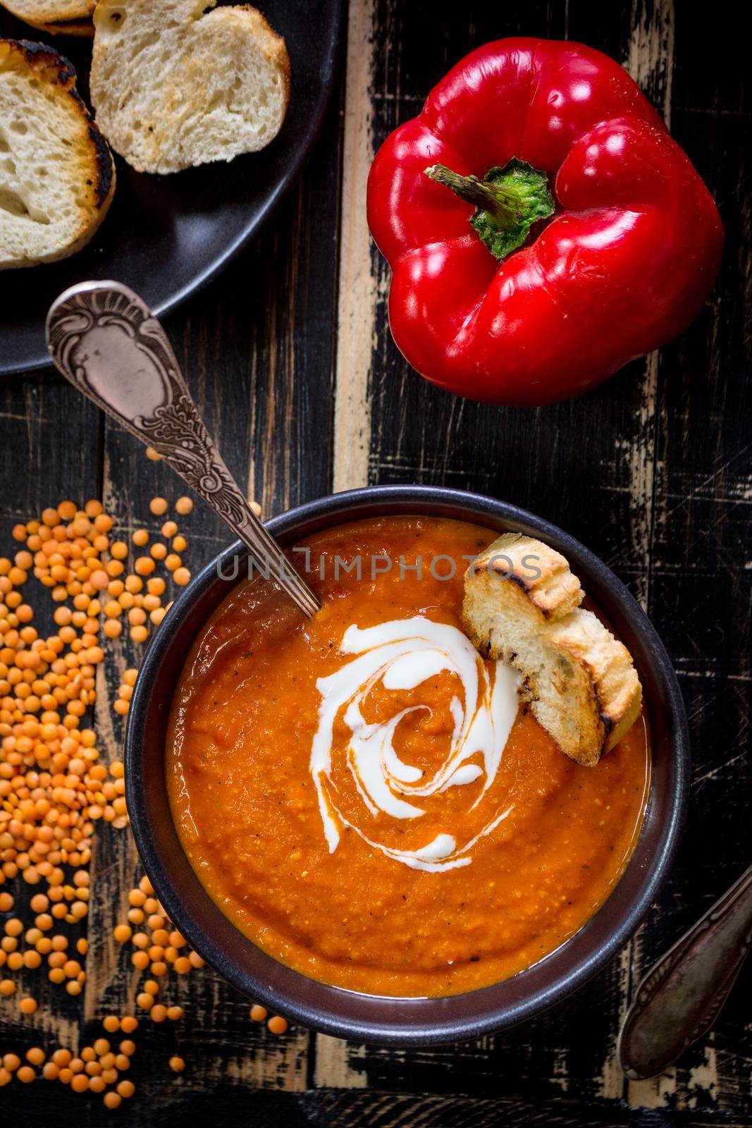 Delicious pumpkin soup with heavy cream on dark rustic wooden table with red bell pepper, bread toasts, lentil. Top view