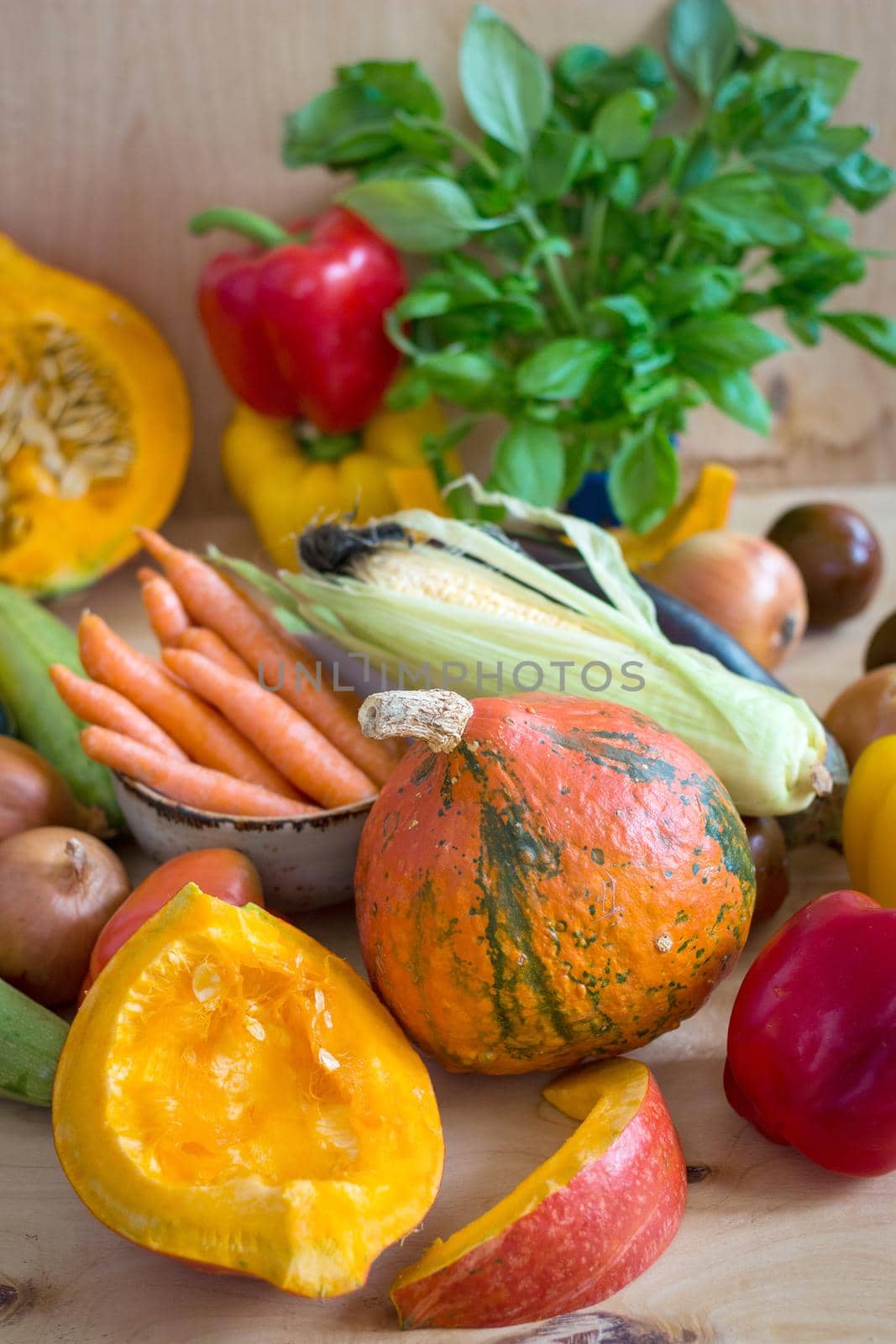 Fresh sliced pumpkin and assorted vegetables. Autumn photo. Healthy eating. Sliced pumpkin, zucchini, squash, bell peppers, carrots, onions, cut garlic, tomatoes, eggplant, corn cob, rucola and basil. Selective focus