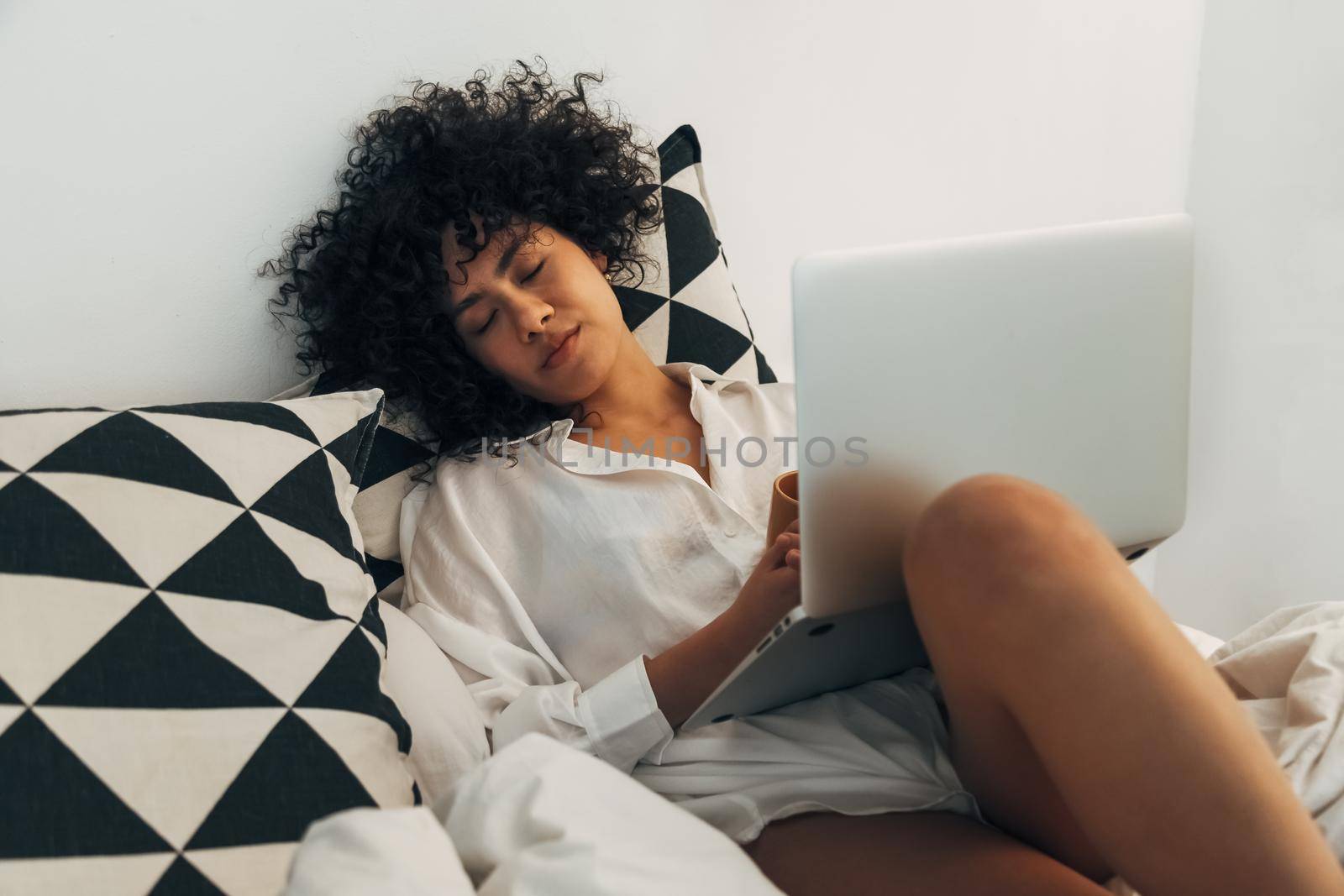 Young african american woman sleeping on bed with laptop. Working late. by Hoverstock