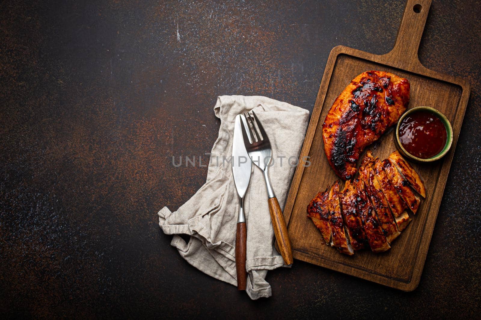 Grilled turkey or chicken marinated fillet with red sauce served and sliced on wooden cutting board on stone brown background from above, poultry breast barbecue space for text