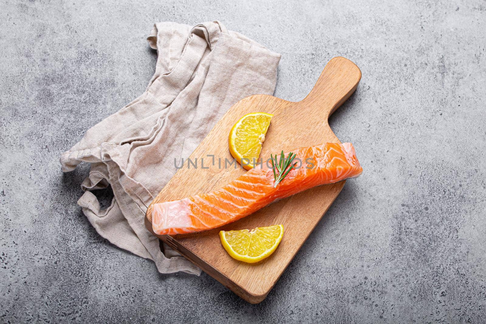 Raw salmon fish fillet with lemon wedges and rosemary on wooden cutting board on gray stone concrete rustic background kitchen table from above, healthy eating and diet