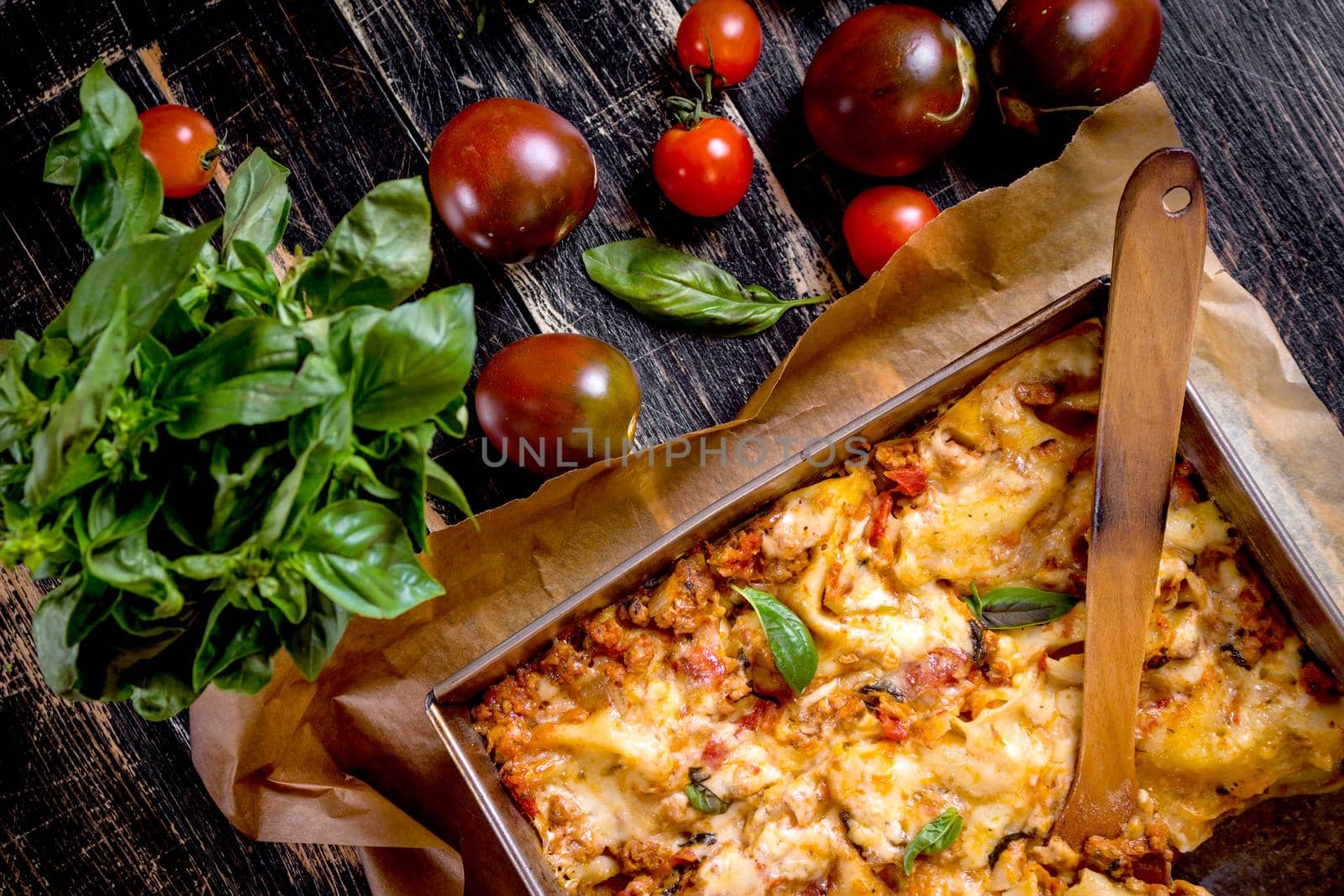 Close-up of a traditional italian lasagna made with minced beef bolognese sauce topped with basil leafs served on a rustic dark wooden table