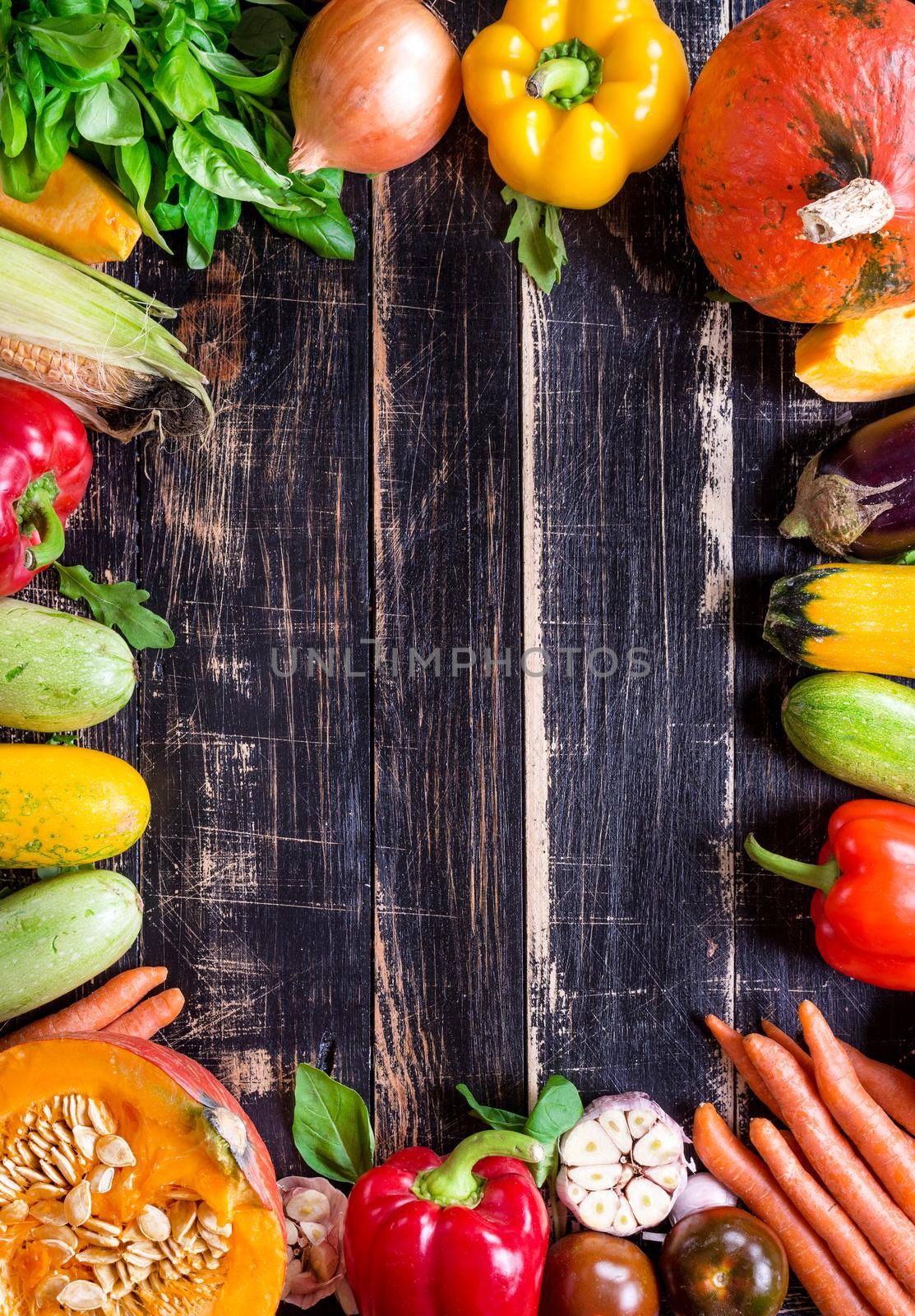 Fresh vegetables on a old rustic dark textured table. Autumn background. Healthy eating frame. Sliced pumpkin, zucchini, squash, bell peppers, carrots, onions, cut garlic, tomatoes, eggplant, corn cob, rucola and basil. Top view. Space for text