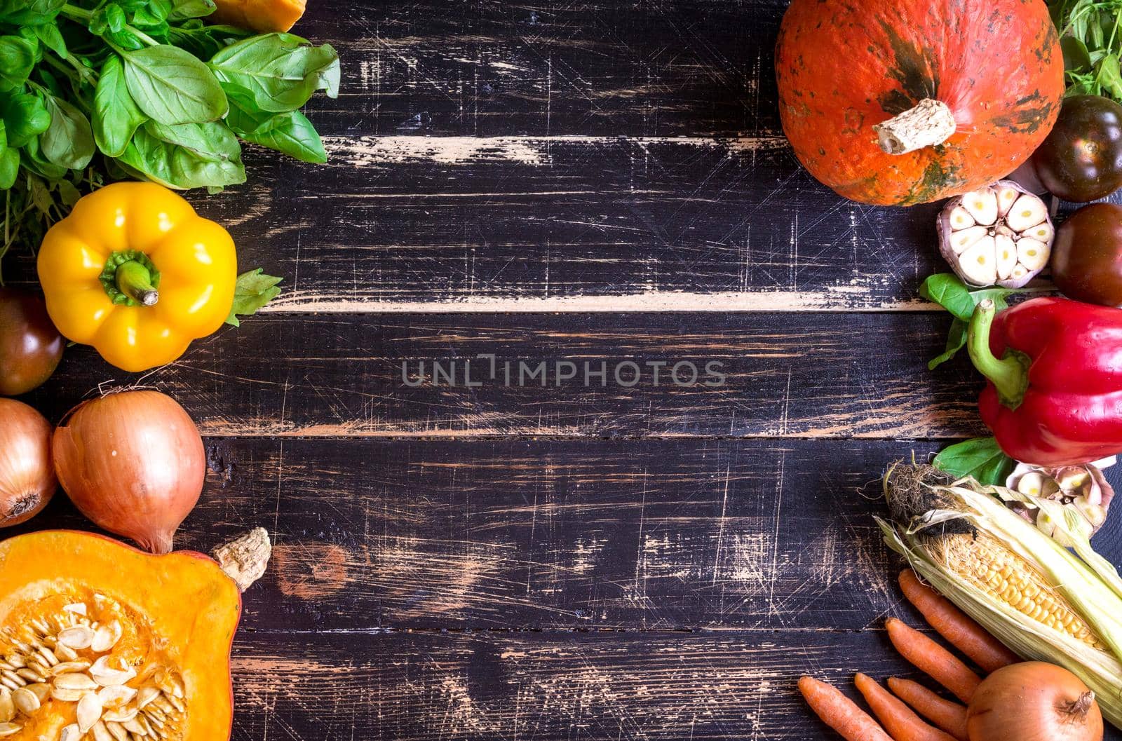 Fresh vegetables on a old rustic dark textured table. Autumn background. Healthy eating frame. Sliced pumpkin, bell peppers, carrots, onions, cut garlic, tomatoes, rucola and basil. Top view. Space for text