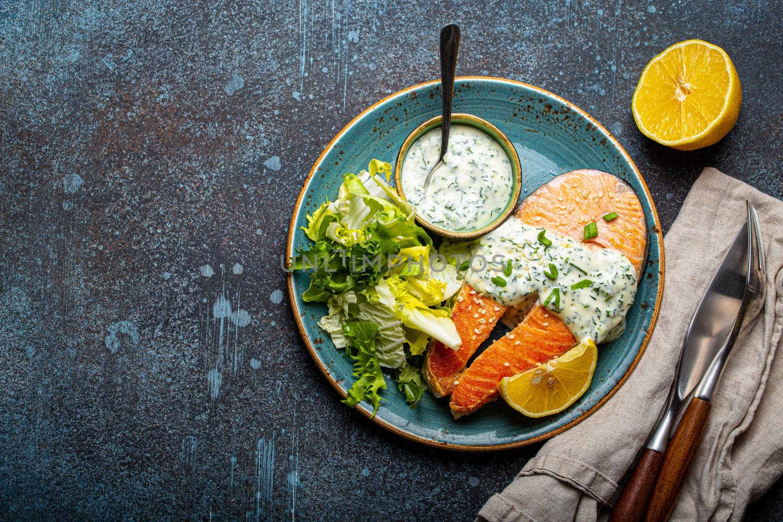 Healthy food meal cooked grilled salmon steaks with white dill sauce and salad leafs on plate on rustic concrete stone background table flat lay from above, diet healthy nutrition dinner copy space