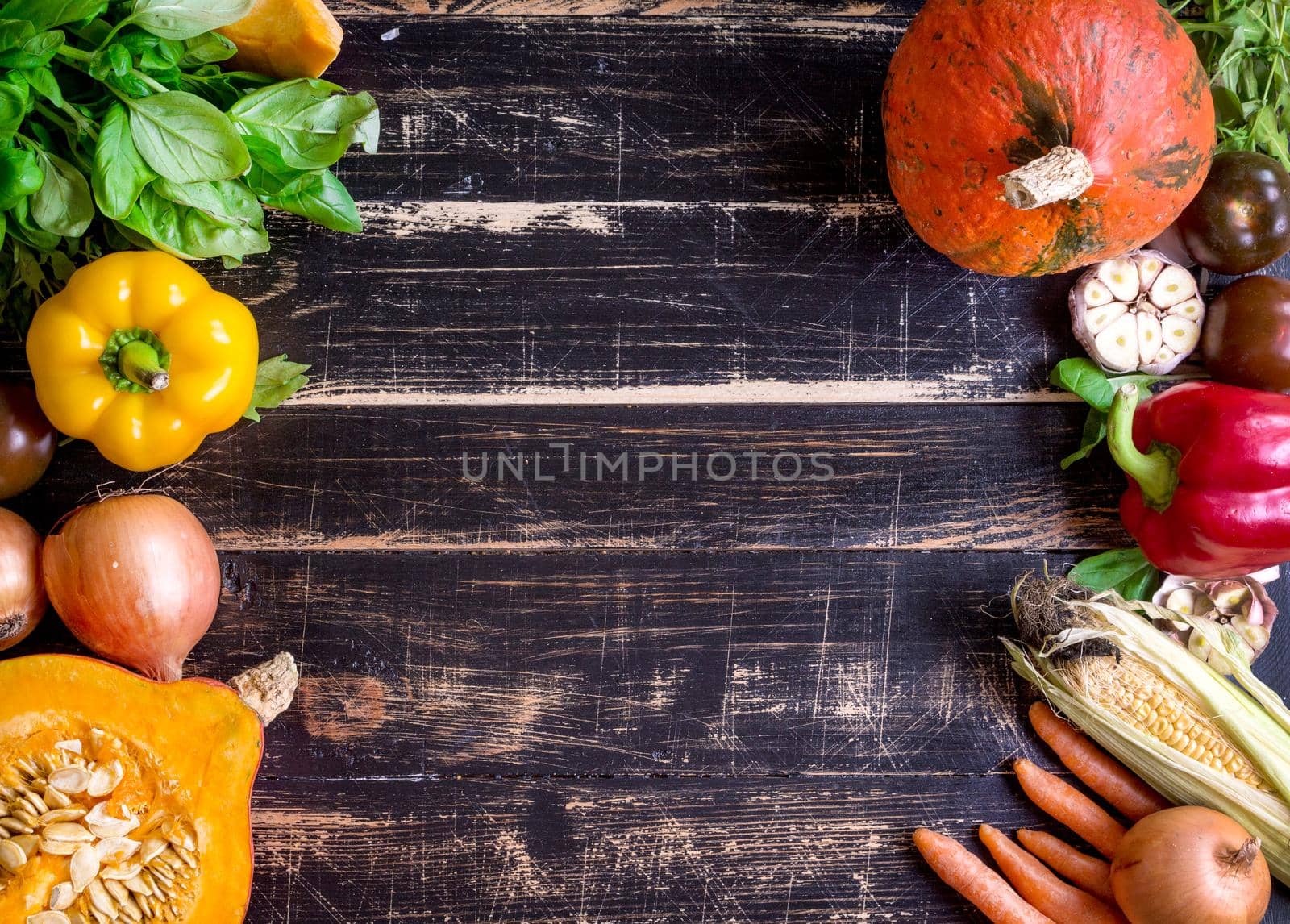 Fresh vegetables on a old rustic dark textured table. Autumn background. Healthy eating frame. Sliced pumpkin, bell peppers, carrots, onions, cut garlic, tomatoes, rucola and basil. Top view. Space for text