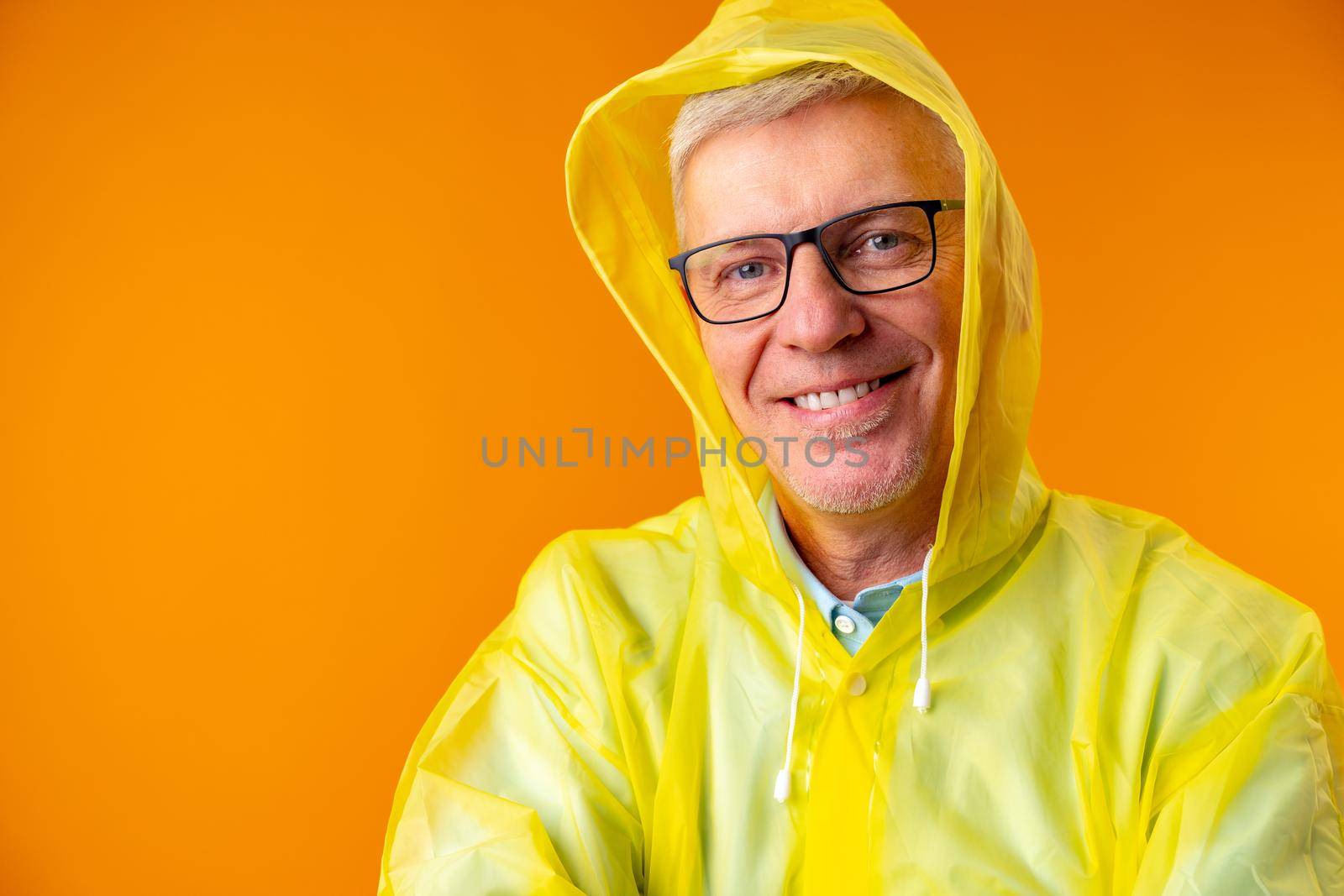 Mature man wearing raincoat over yellow background, portrait
