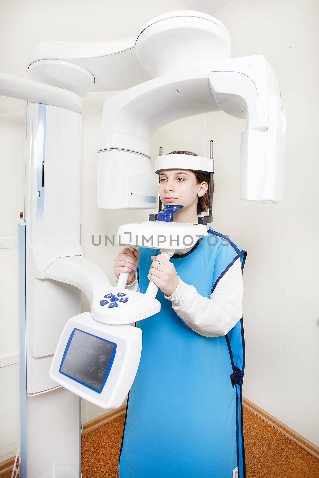 A girl in a protective vest in an X-ray room makes a panoramic picture of her teeth. Rengen equipment in the clinic. by Gravika