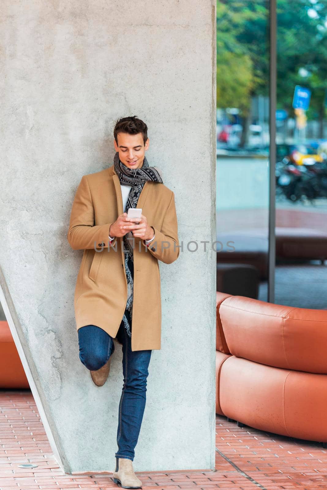 Businessman texting on mobile phone against wall by raferto1973