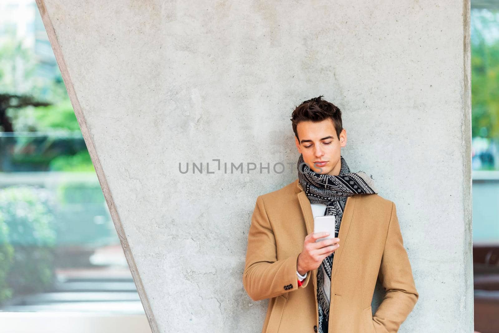 Cheerful man leaning against wall in the city using smartphone